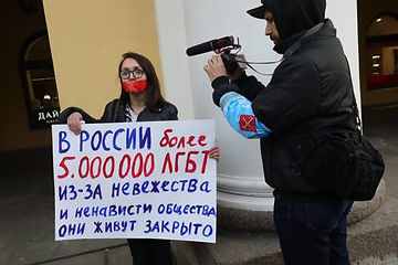 Photo de Yelena en pleine manifestation. Elle est filmée par un vidéaste/journaliste. Elle porte une pancarte écrite en russe.